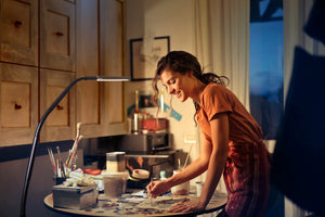 Woman painting at a round table, using the Electra lamp to light her work space.