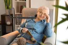 Load image into Gallery viewer, Woman sitting in an arm chair using the Electra lamp to knit.
