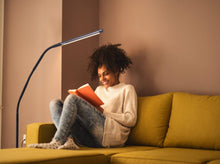 Load image into Gallery viewer, Lady sitting on mustard couch using Electra lamp to read an orange book. 
